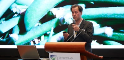 Man speaking into a microphone at a lectern of the European Environment Foundation in front of a large projected photo of plants
