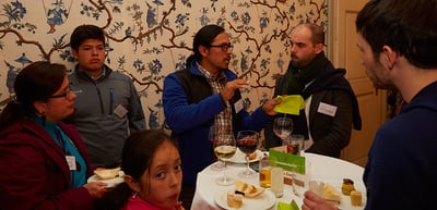 Participants talking at a standing table with drinks and snacks, a girl among them