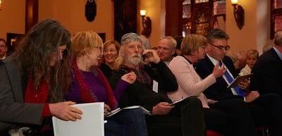 Audience seated in a row reading the programme