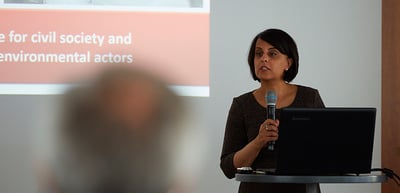 Woman speaking into a microphone in front of a slide about civil society and environmental actors