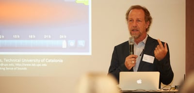 Man speaking into a microphone next to a slide of the Technical University of Catalonia