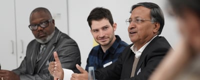 Three participants in a discussion at a table, one of them gesturing while he speaks