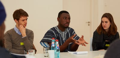 A laureate in a patterned shirt speaking at a round table with students