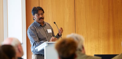 Man speaking at a lectern in a room with wood panelling