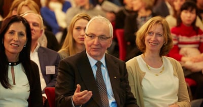 Audience in the front row, an older man in a suit gesturing while he speaks