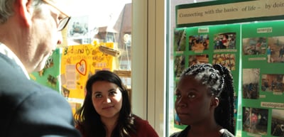 Two young women listening to a man at an exhibition stand with posters