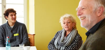 A student, a laureate and a smiling older man at a round table