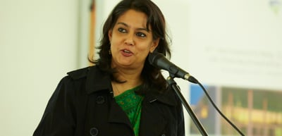 Woman in a black jacket speaking at a microphone stand