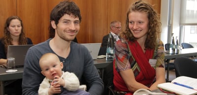 Young man holding a baby next to a smiling young woman at a conference table