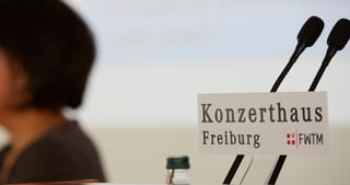 Two microphones and a sign reading "Konzerthaus Freiburg FWTM" on a lectern, a person blurred in the foreground
