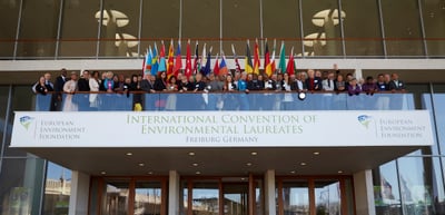 Participants on the balcony of the Konzerthaus Freiburg with national flags above a banner reading "International Convention of Environmental Laureates, Freiburg Germany"
