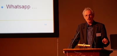 Speaker at a lectern next to a screen showing the word "Whatsapp"