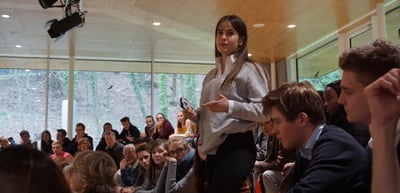 A young woman standing and speaking in front of a seated audience