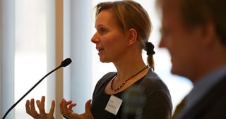 Woman speaking into a microphone and gesturing with both hands