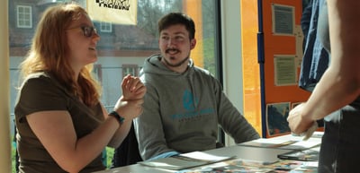 Young woman and young man talking at a table in front of a window