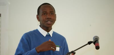 Young man in a blue sweater speaking at a microphone stand