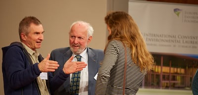 Three participants in conversation in front of a banner of the International Convention of Environmental Laureates