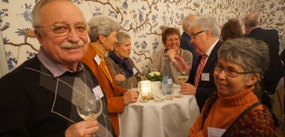 Smiling older man with a wine glass at a dinner table with other participants