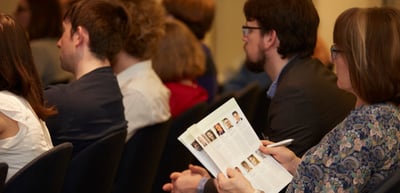 Audience listening, a woman holding a programme with portrait photos