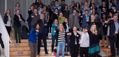 Participants standing on the steps of the hall raising their arms and cheering