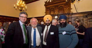 Four men posing for a photo in a historic hall with a chandelier, two of them wearing turbans
