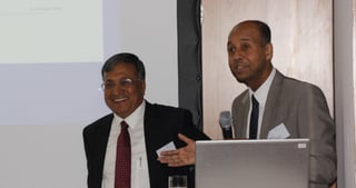 Two men presenting side by side at a lectern with a laptop