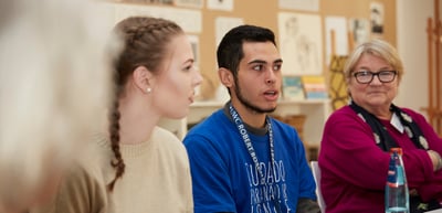 Young man in a blue sweater speaking at a table, a young woman and an older woman next to him