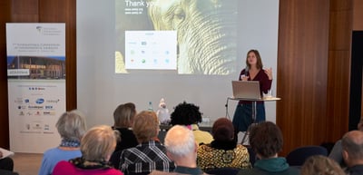 A laureate presenting in front of a projected slide with the text Thank you, next to a roll-up banner of the convention
