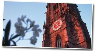 Red sandstone tower of Freiburg Cathedral with its clock against a blue sky