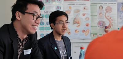 Two smiling young men in a classroom with biology posters