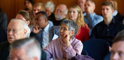 Audience listening in a conference room, a woman with glasses resting her head on her hand