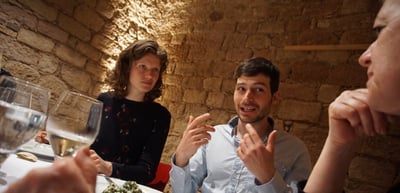 A young man and a young woman talking at a dinner table in a vaulted stone cellar