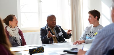 A laureate gesturing as he speaks at a round table with students