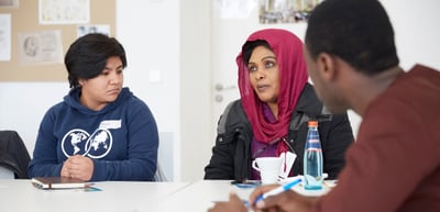 Young woman and a woman in a red headscarf listening to a man at a table