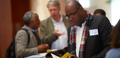 Man in a checked scarf reading a brochure among other participants