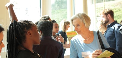 Visitors talking in a crowded room, an older woman holding a brochure