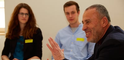A smiling laureate speaking to two students at a round table