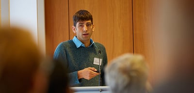Young man in a green sweater speaking at a lectern