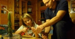 Girl with glasses working on a craft project at a table with a man helping her