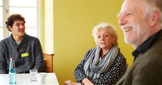 A student, a laureate and a smiling older man at a round table
