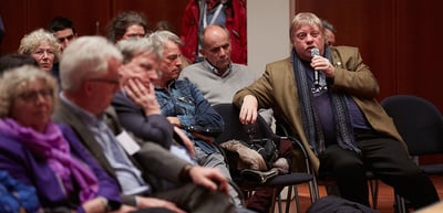 Man in the audience speaking into a microphone, the people around him listening