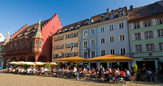 The red Historisches Kaufhaus and colourful houses on the cathedral square in Freiburg, with café tables and parasols
