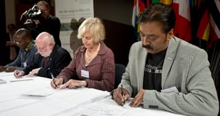 Laureates signing a declaration at a table at the 1st ICEL, a banner in the background reads On the way to Rio+20