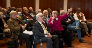 Audience in a hall, a woman in pink asking a question into a microphone