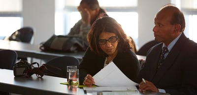 Woman with glasses reading a paper next to a man at a seminar table