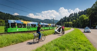 Tram, cyclists, a bicycle taxi and a car on a road in Freiburg with wooded hills