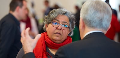Woman with glasses and a red scarf listening to a man
