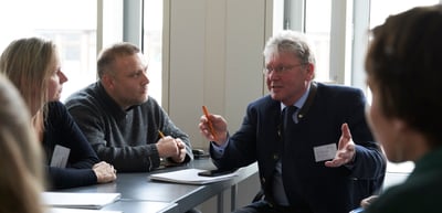 A man gesturing as he speaks at a workshop table