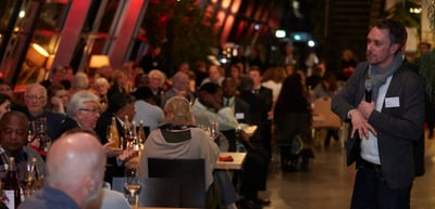 Man speaking into a microphone to the guests in a full restaurant in the evening