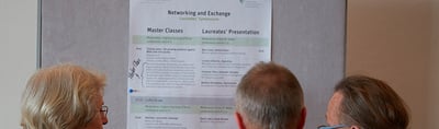 Participants reading the programme "Networking and Exchange, Laureates' Symposium" with the columns Master Classes and Laureates' Presentation on a pin board
